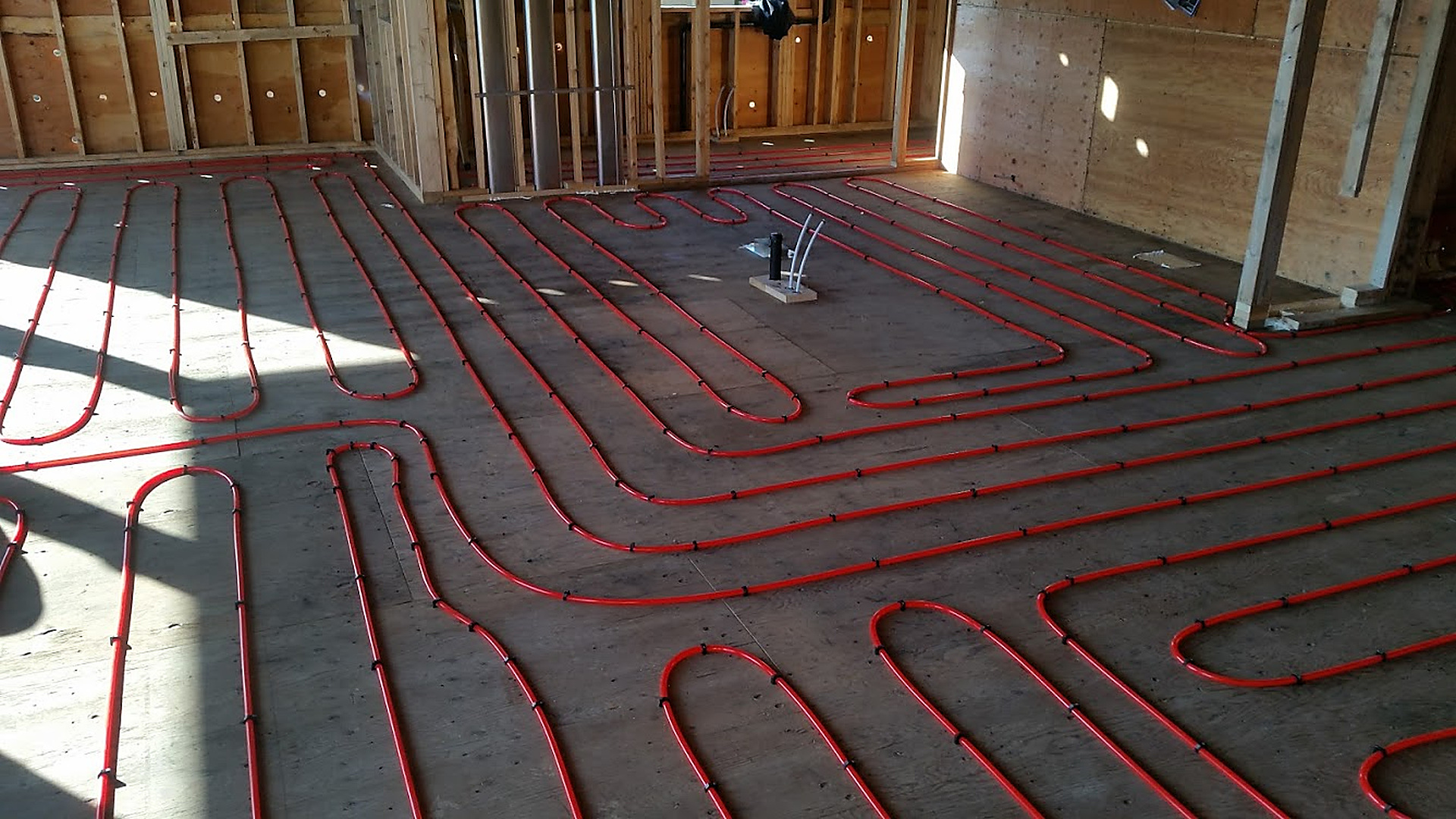 In-Floor Hydronic Heating System — PEX hydronic heating loops fastened across a subfloor in a new build.